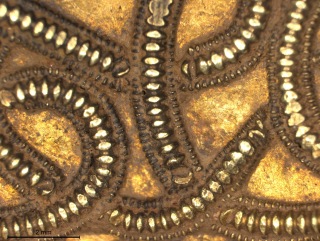 Close-up of Staffordshire Hoard metalwork showing enhanced background beneath filigree overlay